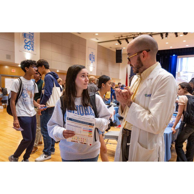 A student talking to an EPA researcher at a Research Week fair inside of a large hall on the campus of UNC-Chapel Hill.